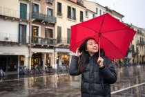 Jovem asiática viajante em roupas quentes sightseeing usando guarda-chuva vermelho com edifícios antigos no fundo borrado em Padova na Itália — Fotografia de Stock