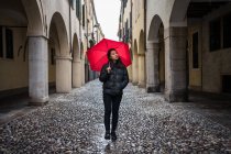 Junge asiatische Reisenden in warmer Kleidung Sightseeing mit rotem Regenschirm mit alten Gebäuden auf verschwommenem Hintergrund bei Padova in Italien — Stockfoto