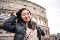Von brüllend glückliche Frau lächelnd und in die Kamera blickend, während sie auf verschwommenem Hintergrund des Kolosseums auf der Straße von Rom, Italien steht — Stockfoto