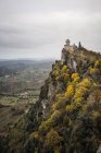 Castelo antigo em pico coberto com árvores verdes erguendo-se alto em céu cinza em San Marino, Itália — Fotografia de Stock