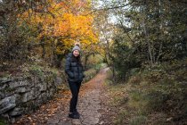 Junge, charmante Asiatin in schwarzer, warmer Jacke und Strickmütze mit Bommel, lächelnd und in die Kamera blickend im Garten mit Herbstblättern in San Marino, Italien — Stockfoto