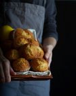 Crop person in grembiule dray con vassoio marrone pieno di muffin appena sfornati — Foto stock