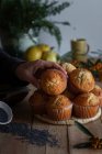Аппетитные свежие выпеченные кексы на плетеной стойке на деревянном столе, украшенном ягодами лимона и мака семена для выпечки — стоковое фото