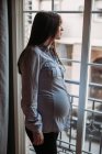 Mulher grávida olhando para a janela em casa — Fotografia de Stock