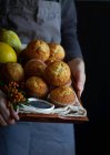 Crop person in grembiule dray con vassoio marrone pieno di muffin appena sfornati — Foto stock