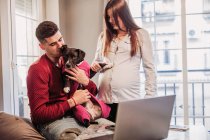 Young couple expecting baby having fun with dog at home — Stock Photo