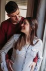 Schwangere Frau mit Ehemann schaut zu Hause auf Fenster — Stockfoto