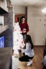 Casal jovem esperando bebê arranjando árvore de Natal em casa — Fotografia de Stock