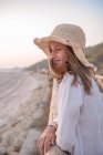 Charming woman in hat leaning on fence and looking at sea — Stock Photo