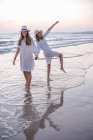 Sonrientes novias en ropa de verano descalzas en el agua en la playa - foto de stock