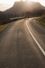 Corridori maschi sani attivi che corrono insieme su strada asfaltata curva con luce solare da dietro la montagna sullo sfondo — Foto stock