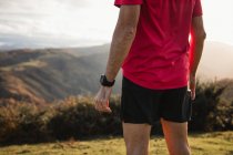 Vista posterior del hombre deportivo en camisas azules y rojas de pie en la cima de una colina verde y disfrutando del paisaje - foto de stock