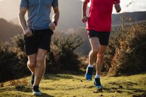 Cropped image of strong active males in sportswear running together on green grass in mountains in sunny autumn day — Stock Photo
