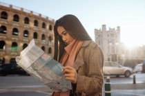 Jeune femme asiatique en vêtements élégants examinant la carte tout en visitant la ville historique le jour ensoleillé — Photo de stock