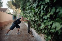 Elderly man stretching on botanical wall in street — Stock Photo