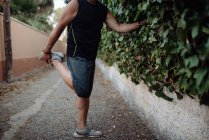 Літній чоловік розтягує ногу, тримаючи ботанічну стіну на вулиці — стокове фото
