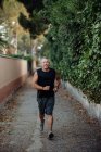 Старий у добрій формі біжить по дорозі вздовж огорожі рослин — стокове фото
