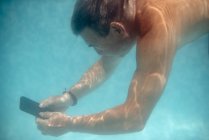 Homem maduro mergulho debaixo de água com smartphone — Fotografia de Stock