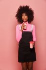 Felice donna nera con tazza monouso di bevanda in piedi contro sfondo rosa — Foto stock