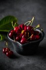 Сверху натуральные сочные спелые вишни с красным цветком в миске за серым столом в помещении — стоковое фото