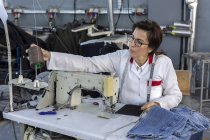 Mulher trabalhadora na costura de fábrica têxtil na máquina de costura industrial. Produção industrial — Fotografia de Stock