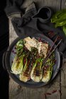 Top view of plate with yummy bok choy salad and fried fish placed near napkin on wooden table — Stock Photo