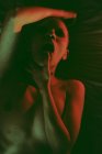 Сексуальная горячая страстная обнаженная женщина с бритой головой, лежащей в постели с пальцем в рот в темной студии с красным светом — стоковое фото