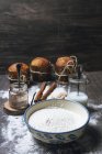 Bowl with white flour and glass jars with cocoa powder and milk placed on table next to spices and baked panettones — Stock Photo