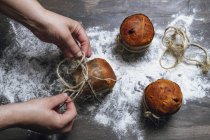 Hands of person decorating panettones with twine on table dusted with flour — Stock Photo