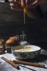 Hände der Person brechen Ei in Schüssel auf Holztisch mit Zimt und Vanille und gebackenen Kuchen platziert — Stockfoto