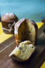 Gâteaux panettone de Noël artisanaux frais coupés avec des raisins secs sur une planche de bois placée sur une table jaune contre un mur bleu — Photo de stock