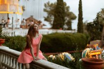 Молодая женщина в розовом платье сидит на заборе в парке развлечений — стоковое фото