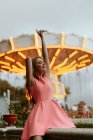 Молодая женщина в розовом платье сидит на заборе в парке развлечений — стоковое фото
