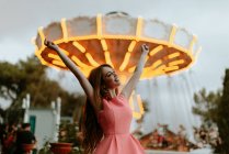 Молода жінка в рожевій сукні сидить на паркані в парку розваг — стокове фото