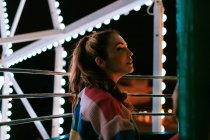 Young woman riding luminous Ferris wheel in summer night — Stock Photo