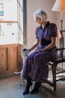 Calma donna anziana seduta in poltrona con cane nella stanza della luce — Foto stock
