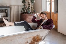 Прохладный элегантный босиком мятежник расслабляется в ванне против винтажного интерьера в загородном доме — стоковое фото