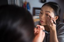 Asian woman applying eyeliner in front of mirror — Stock Photo