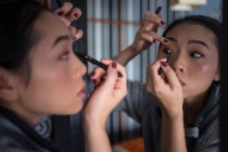 Asiatico donna applicando eyeliner di fronte a specchio — Foto stock