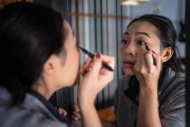 Asian woman applying eyeliner in front of mirror — Stock Photo
