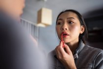 Jeune femme appliquant du rouge à lèvres devant le miroir — Photo de stock