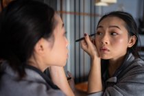 Mulher asiática aplicando eyeliner na frente do espelho — Fotografia de Stock