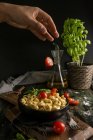 Man adding tomatoes to bowl with ravioli — Stock Photo