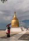 Woman with traditional umbrella walking next to Buddhist pagoda — Stock Photo