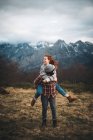 Lovely couple hugging and spending time together piggybacking and traveling in lawn with dry grass near by mountains in cloudy day — Stock Photo
