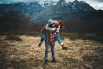 Lovely couple hugging and spending time together piggybacking and traveling in lawn with dry grass near by mountains in cloudy day — Stock Photo