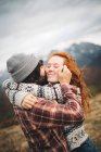 Seitenansicht eines zarten Paares, das sich an kalten Tagen in den Bergen mit geschlossenen Augen umarmt und klebt — Stockfoto