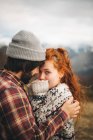 Seitenansicht eines zarten Paares, das sich umarmt und bindet, mit geschlossenen Augen und einer Frau, die an kalten Tagen in den Bergen in die Kamera blickt — Stockfoto