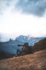 Vue latérale du photographe itinérant avec sac à dos prenant des photos assis sur le sol dans les montagnes — Photo de stock