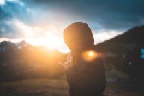 Вид збоку мандрівника в куртці з капюшоном насолоджується пейзажем гори на сонячному світлі — стокове фото